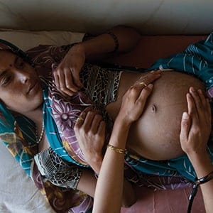 A pregnant woman lies on an examination table as a nurse places her hands on her stomach during a check up at a community health centre in Chharchh