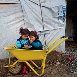 © Mohammad Husein, 15 years old when the workshops began. Syrian Refugee Camp, Kawergosk, Kurdistan, Iraq.
Photograph created as part of the five-year project Exile Voices, launched in December 2013 by Reza to train refugee children in the camps in photography.
Mohammad Husein, aged 17, captures two little girls playing in a wheelbarrow at the Kawergosk refugee camp. Despite adversity, children continue to play and live.