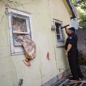 A Regina Fire Department official with the Housing Standards Enforcement Team looks into the window of an abandonned house in Regina's notorious North Central neighbourhood on August 24, 2006. Empty houses are often occupied by squatters for drug activity. (Photograph by Simon Hayter)