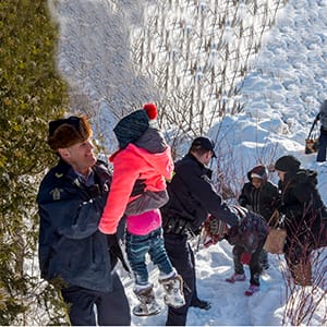Family members from Somalia are helped into Canada by RCMP officers along the U.S.-Canada border near Hemmingford, Que., on Friday, February 17, 2017. A number of refugee claimants are braving the elements to illicitly enter Canada. (Paul Chiasson/CP)