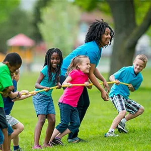 Kids and counselors playing tug of war at summer camp. (FatCamera/iStock)