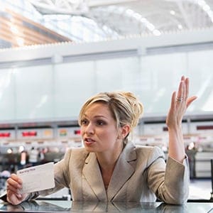 Upset businesswoman checking in at airport ticket counter. (Jupiterimages)