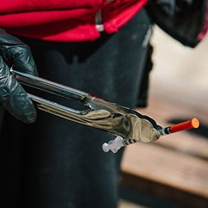 A used needle is picked up with tongs from the sidewalk in downtown Vancouver. (Photograph by Jackie Dives)