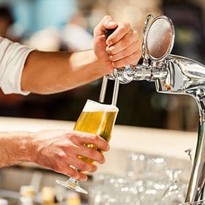 Pouring fresh beer. Close-up of young bartender pouring beer while standing at the bar counter (G-Stock Studio/Shutterstock)