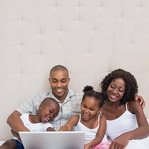 Happy family using laptop together on bed at home in the bedroom. (Wavebreakmedia/Shutterstock)