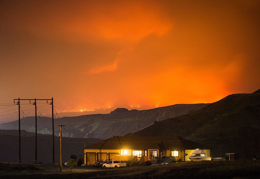 A wildfire burns on a mountain in the distance east of Cache Creek behind a house in Boston Flats, B.C., in the early morning hours of Monday July 10, 2017. (Darryl Dyck/CP)