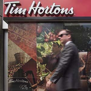 Pedestrians walk past a Tim Hortons coffee shop in downtown Toronto on Wednesday, June 29, 2016. Employees at the Tim Hortons locations owned by the children of the co-founders of the franchise say they have reduced employee benefits and cut back paid breaks to help offset Ontario's $2.40 jump in hourly minimum wage. THE CANADIAN PRESS/Eduardo Lima