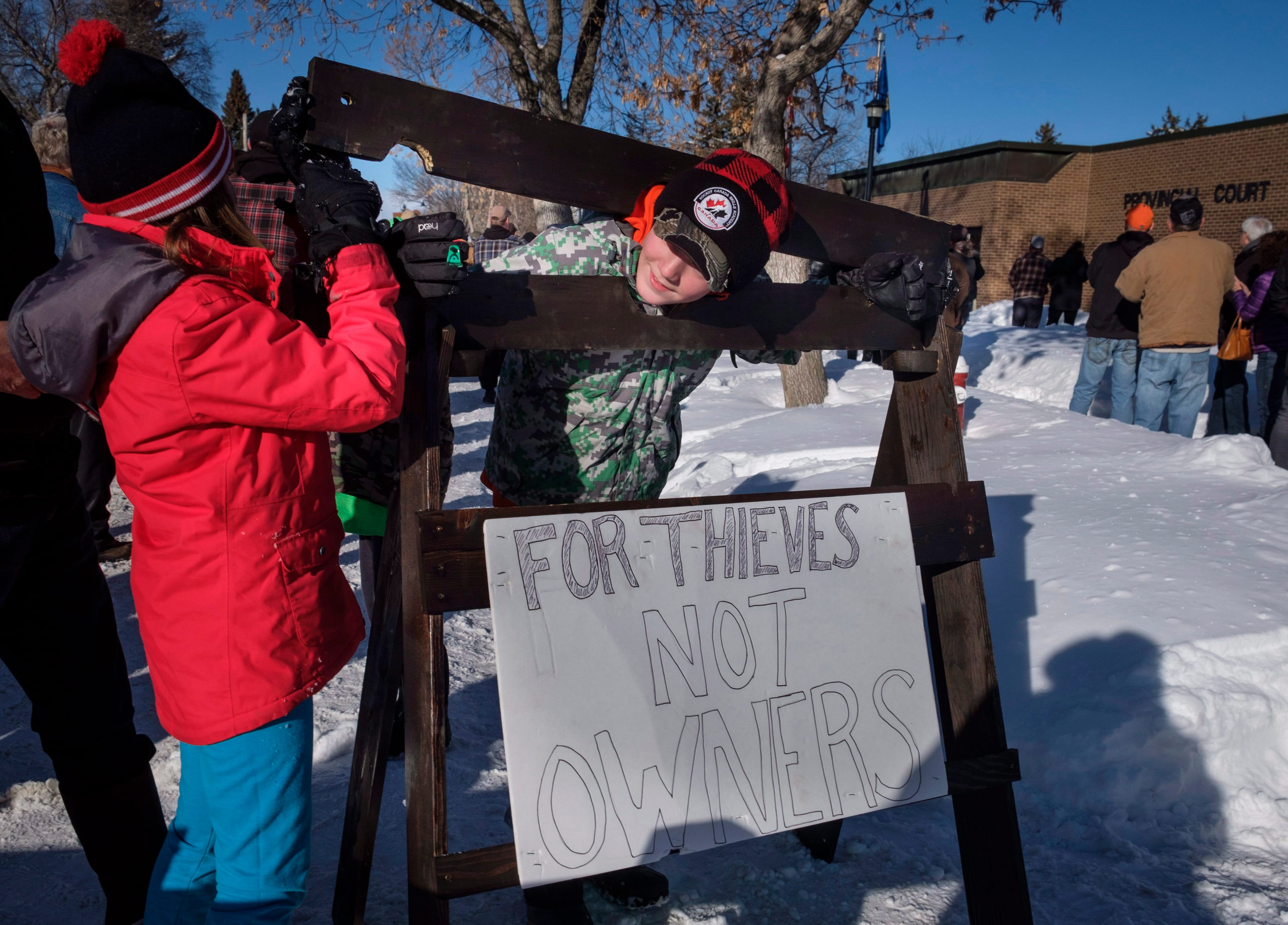 A young boy and girl play with homemade stocks as people gather in support of Edouard Maurice, who faces three charges after police allege the rural homeowner confronted two people rummaging through his vehicles and shots were fired, outside court in Okotoks, Alta., Friday, March 9, 2018. THE CANADIAN PRESS/Jeff McIntosh