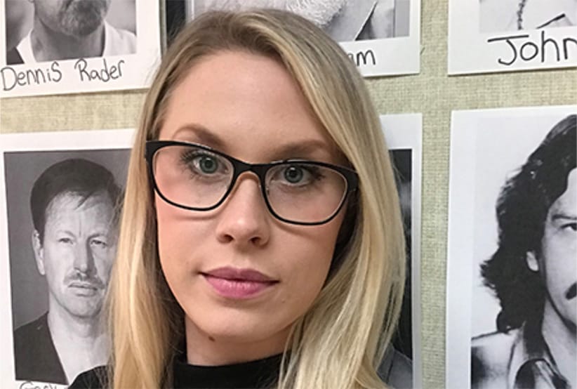 Sasha Reid stands before a board of photos of prolific serial killers in her office at the University of Toronto (Photo: Courtesty of Sasha Reid)