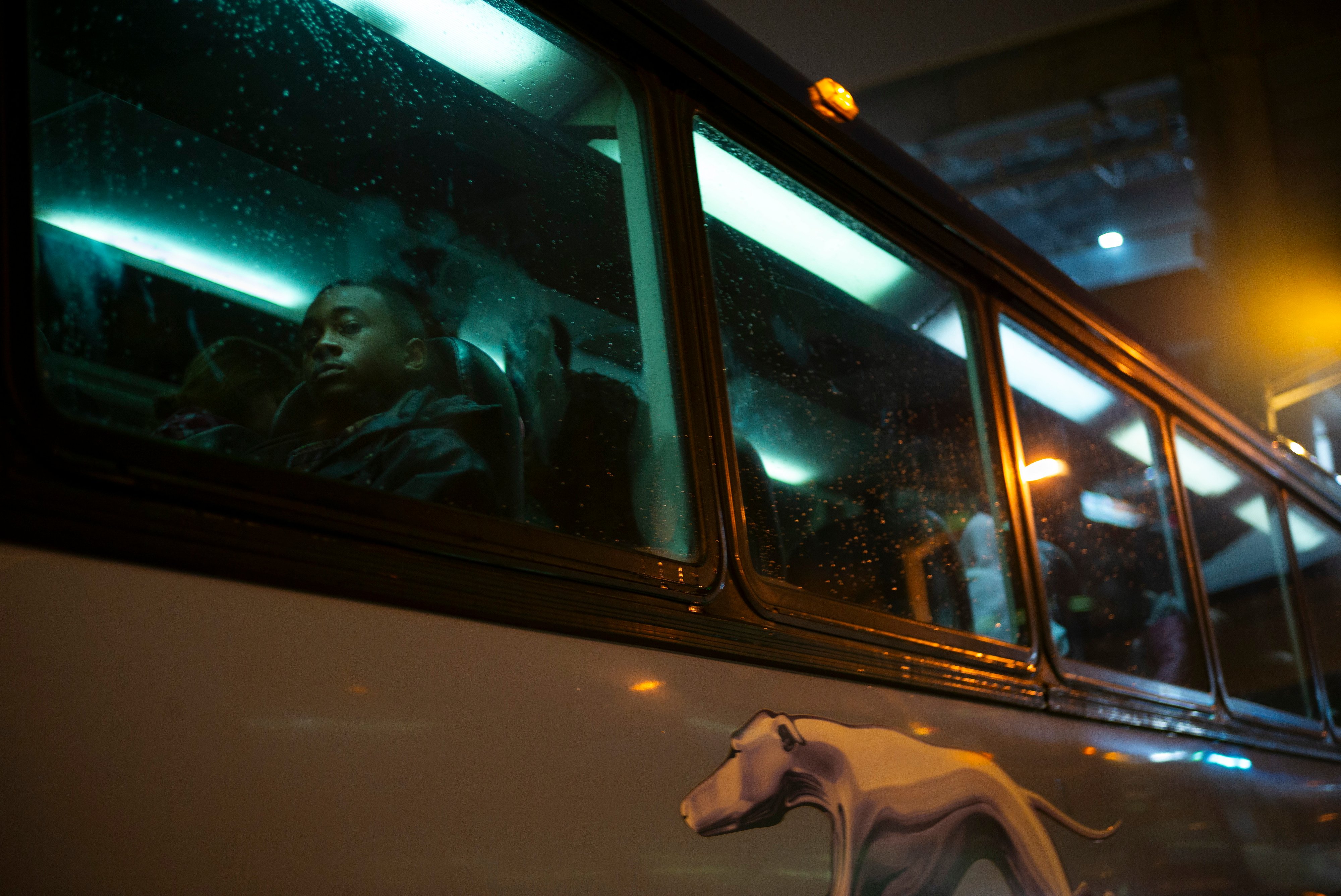 A young man seated on a Greyhound bus, photographed from outside the bus