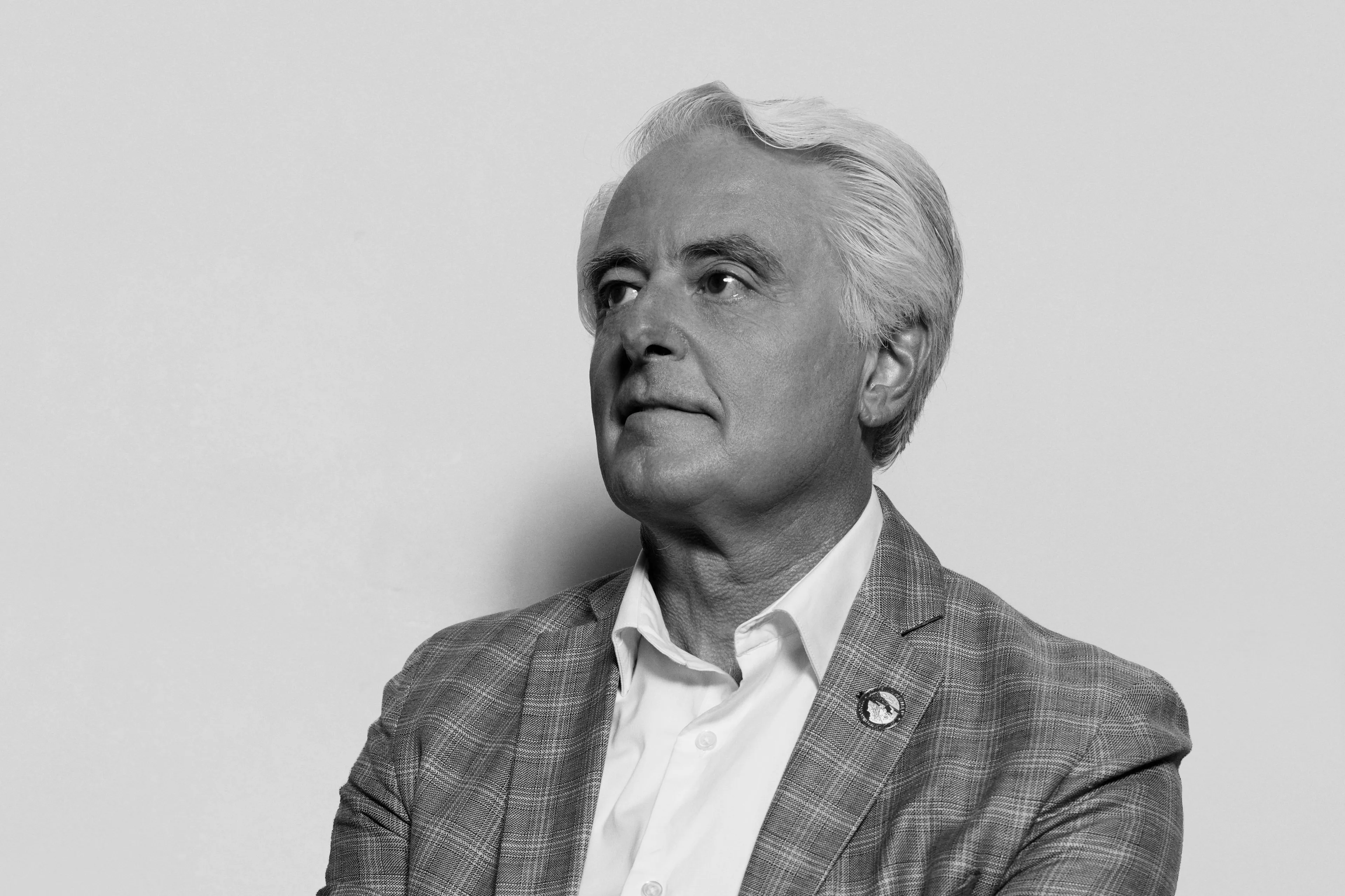 A man in a plaid blazer and white dress shirt looking off to the side
