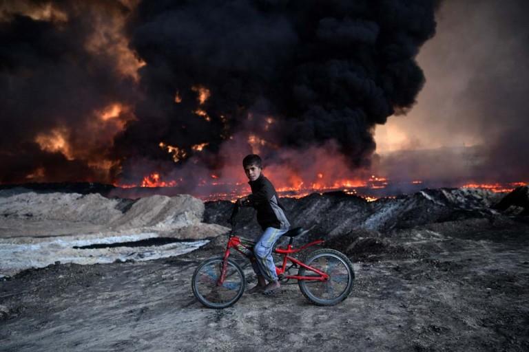 <p>A boy pauses on his bike as he passes an oil field that was set on fire by retreating ISIS fighters ahead of the Mosul offensive, on October 21, 2016 in Qayyarah, Iraq. Several hundred Iraqi families have been made to leave their homes for Mosul by Islamic State fighters as the UN warns they could be used as human shields. ISIS have attacked Kirkuk today as Kurdish and Iraqi forces, backed by a coalition including Britain and the U.S.A continue their offensive to retake Iraq&#8217;s second largest city of Mosul.  (Carl Court/Getty Images)</p>
