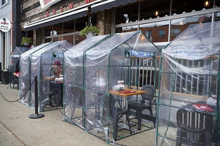 People sit outdoors for drinks under a clear plastic structure on The Danforth in Toronto on Oct. 31, 2020, as the city navigates a modified Stage 2 amid the ongoing COVD-19 pandemic. (Rachel Verbin/CP)
