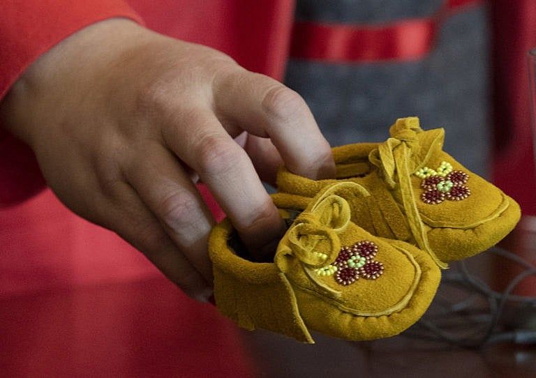 AFN Regional Chief Cindy Woodhouse picks up a pair of children’s moccasins she had placed on her desk at a news conference, Jan. 4, 2022 in Ottawa. (Adrian Wyld/The Canadian Press)