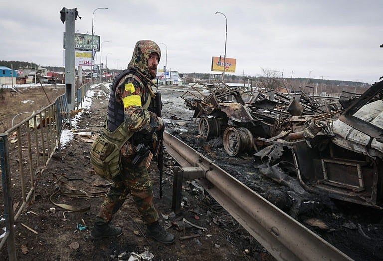 An armed man stands by the remains of a Russian military vehicle in Bucha, close to the capital Kyiv, Ukraine, on March 1, 2022 (AP Photo/Serhii Nuzhnenko)