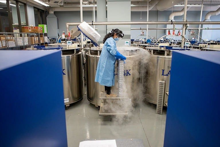 woman standing in a blue lab coat with gas emerging from steel circular containers