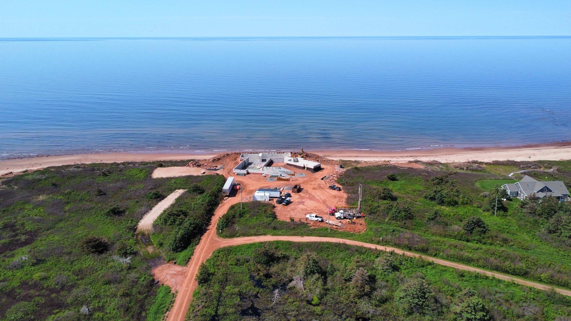 An incomplete compound under construction, with blue ocean in the background and forested areas in the foreground.