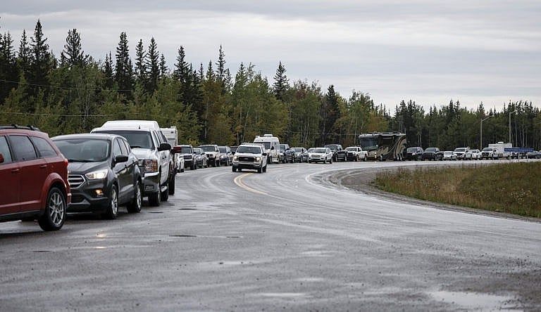 A line of cars and trucks wait in standstill traffic on a curved wet road.