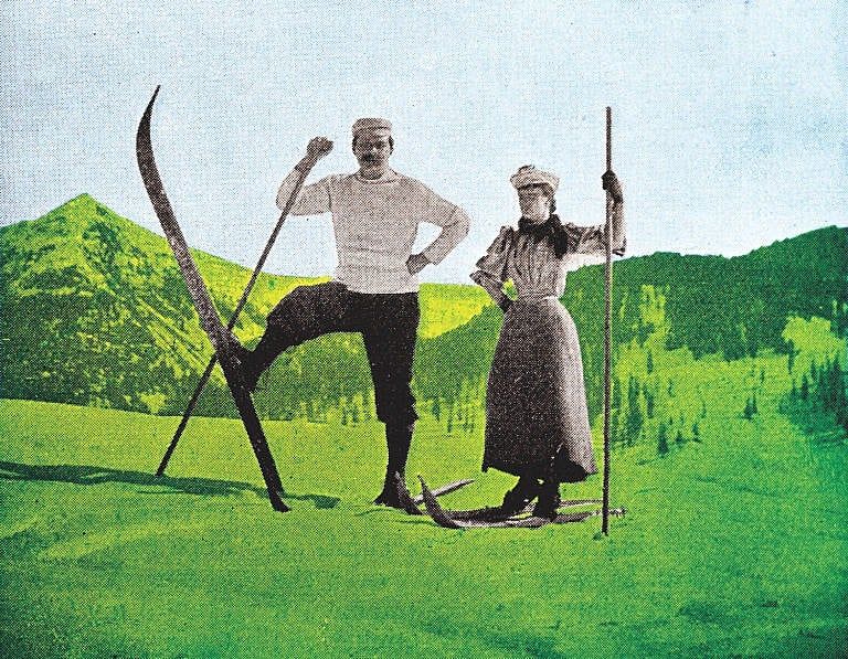 A photo of a man and a woman in skiing gear, standing in front of a green mountain