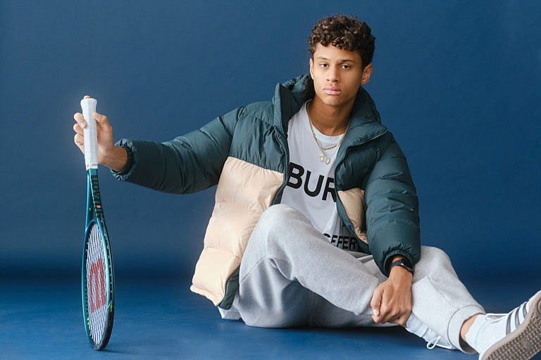 A boy in a jacket and sweatpants holding a tennis racket