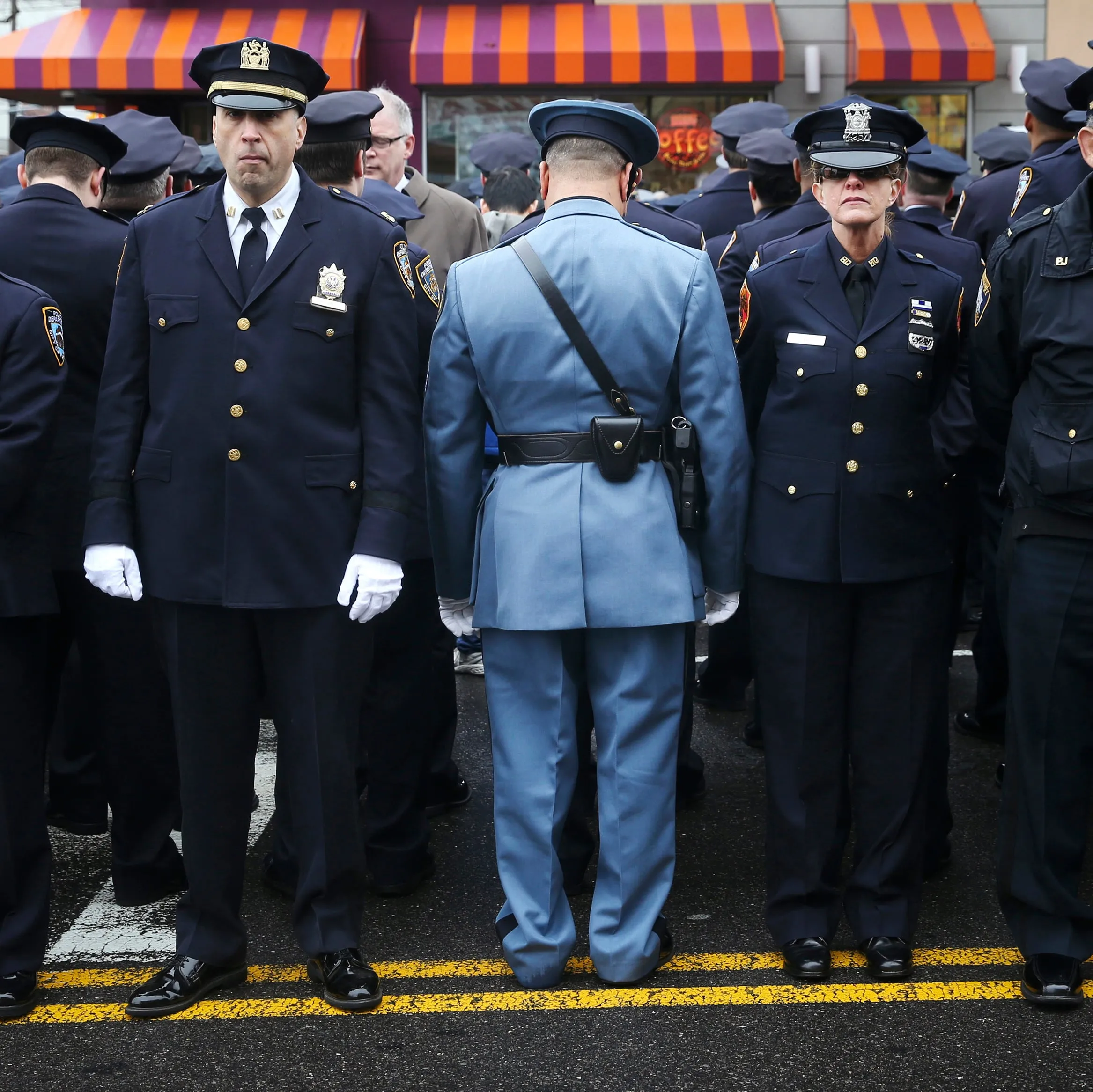 Law enforcement officers stand, with some turning their backs, as New York City Mayor Bill de Blasio speaks on a monitor outside the funeral for NYPD officer Wenjian Liu in the Brooklyn borough of New York
