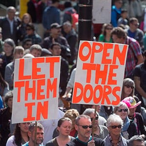 People hold signs as hundreds gather for a rally organized by the local Kurdish community to call on the Canadian government to allow more Syrian refugees into the country, in Vancouver, B.C., on Sunday, September 6, 2015. THE CANADIAN PRESS/Darryl Dyck