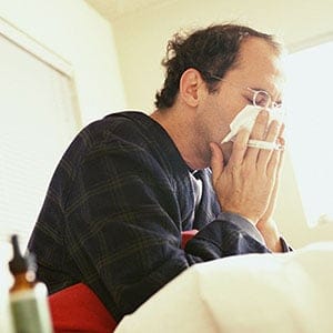 Man sick in bed blowing his nose. Marc Romanelli/Getty Images