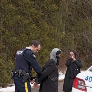 Two women claiming to be from Yemen are detained by a Royal Canadian Mounted Police (RCMP) officer after crossing the U.S.-Canada border into Hemmingford, Quebec on February 22, 2017. (Christinne Muschi/Reuters)