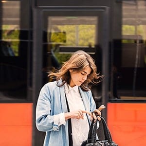 Young woman using mobile phone against bus. (Maskot/Getty)