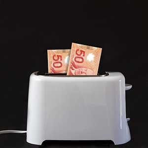 Dollar bills in a white toaster, about to be burned. Copy space available.