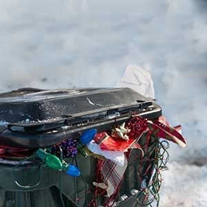 a large plastic trashbin overflowing with garbage and discarded Christmas paper lights bows etc