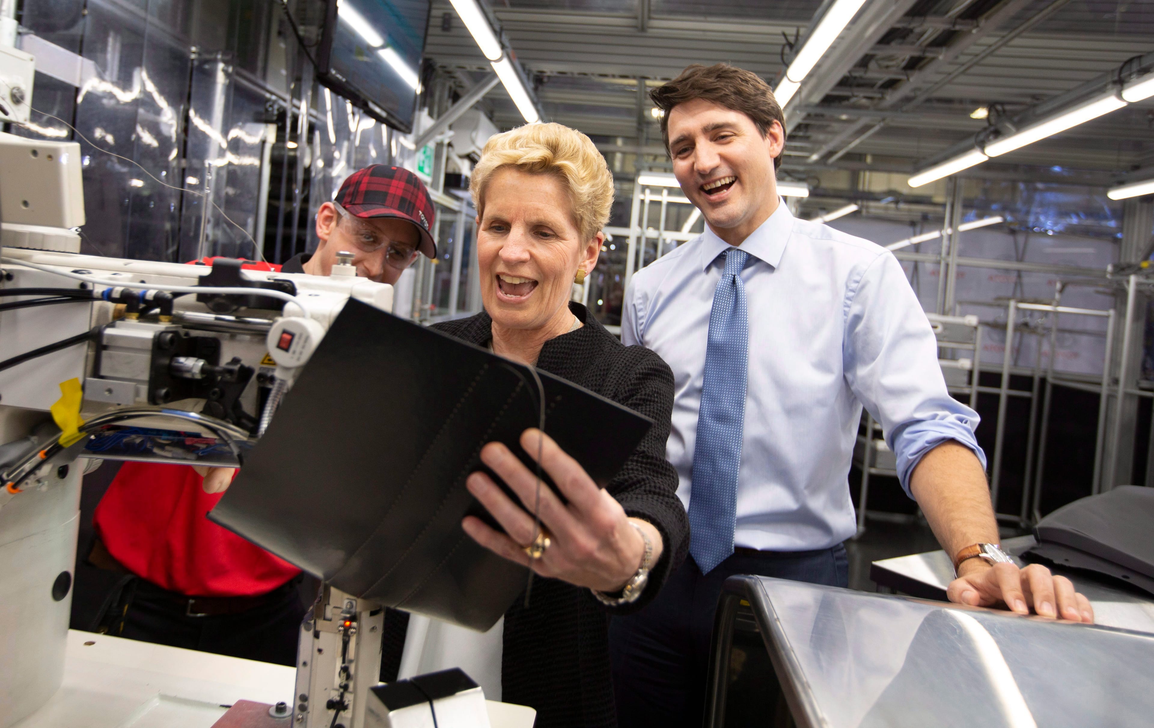 Prime Minister Justin Trudeau and Ontario Premier Kathleen Wynne laugh while trying their hand at leather stitching during their visit to the TMMC Toyota Manufacturing facility in Cambridge, ON on Friday, May 4, 2018. (THE CANADIAN PRESS/Peter Power)
