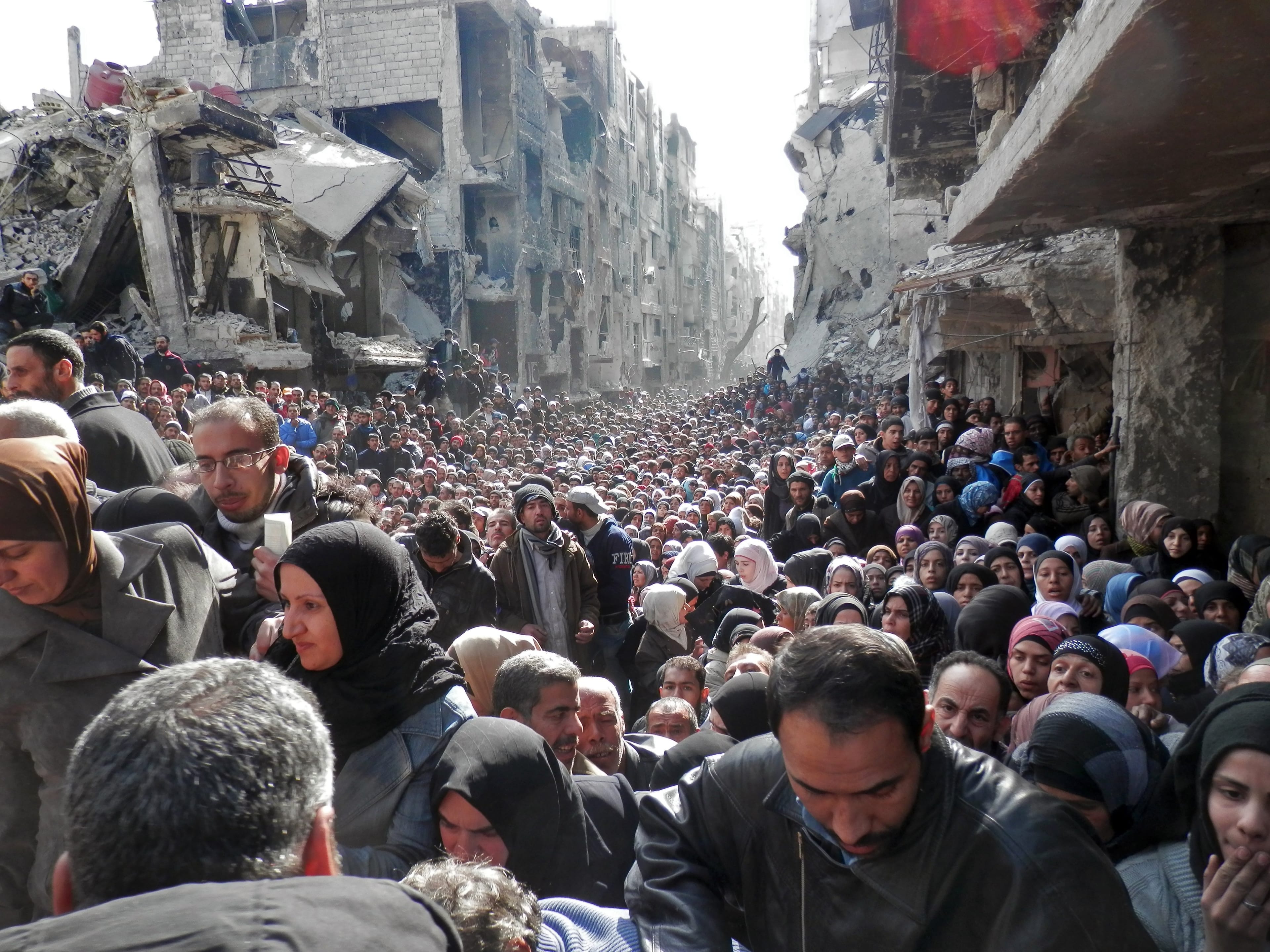 In this handout provided by the United Nation Relief and Works Agency (UNRWA), residents wait in line to receive food aid distributed in the Yarmouk refugee camp on January 31, 2014 in Damascus, Syria. (Photo by United Nation Relief and Works Agency via Getty Images)