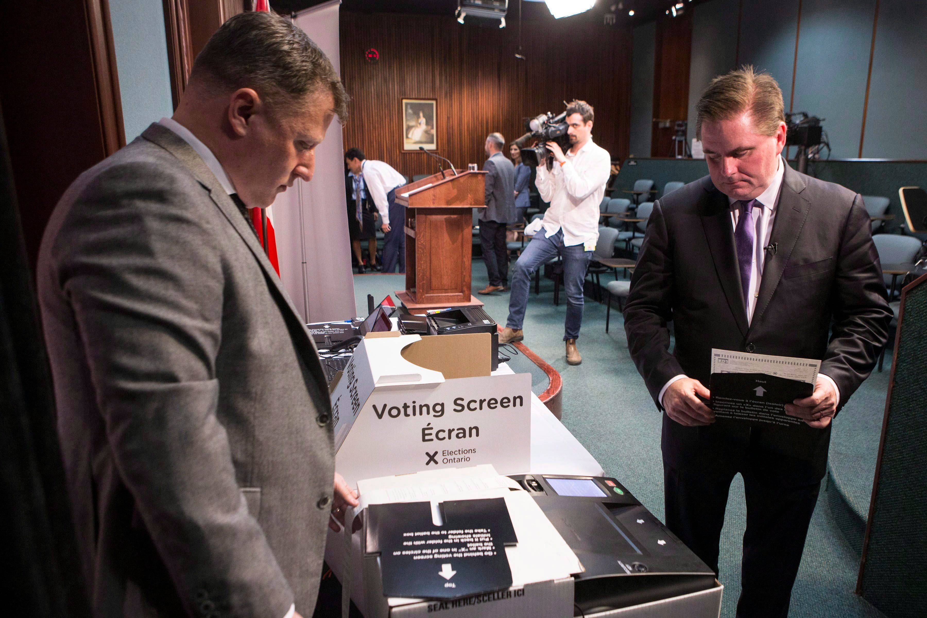 Ontario's Chief Electoral Officer Greg Essensa (right) takes a ballot to a vote tabulator as he demonstrate an electronic voting machine during a media availability in Toronto on Wednesday May 9 , 2018. THE CANADIAN PRESS/Chris Young