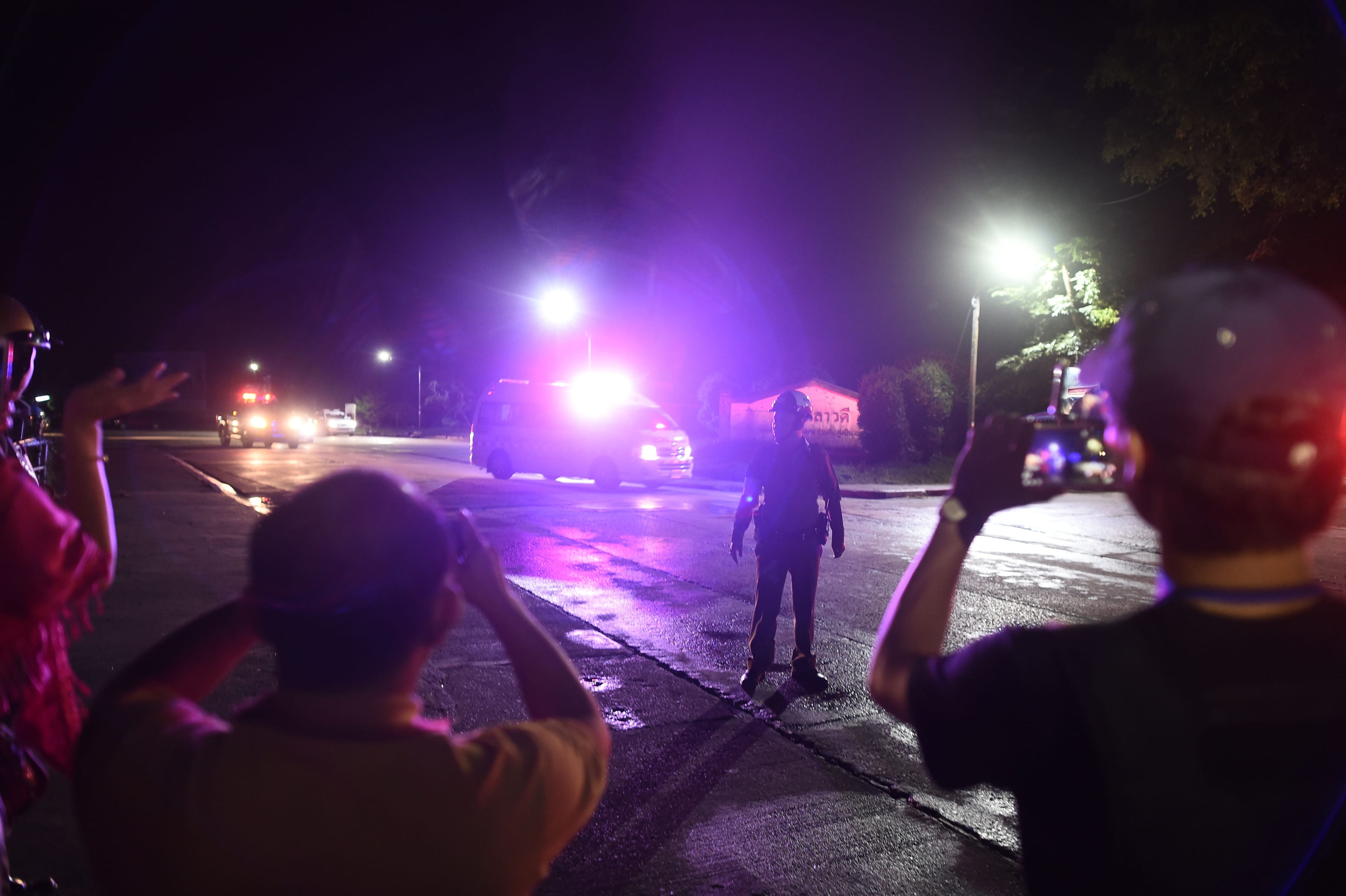 People watch as an ambulance with escort are seen leaving the military airport in Chiang Rai to a nearby hospital after taking passengers from a helicopter as divers evacuated some of the 12 boys and their coach trapped at Tham Luang cave. (Photo by Ye Aung Thu / AFP)