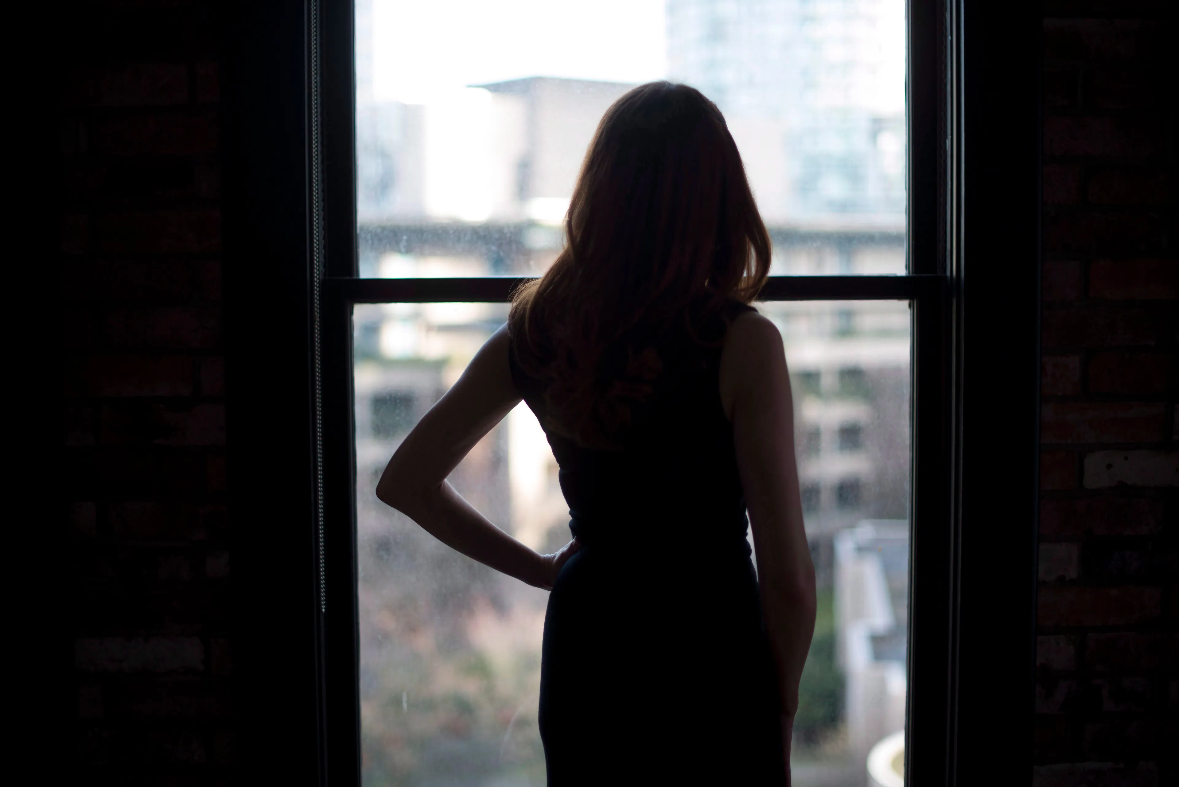 An escort who gave her name as SB is silhouetted against a window as she poses at a downtown Vancouver apartment, Feb. 12, 2017. (Jonathan Hayward/CP)