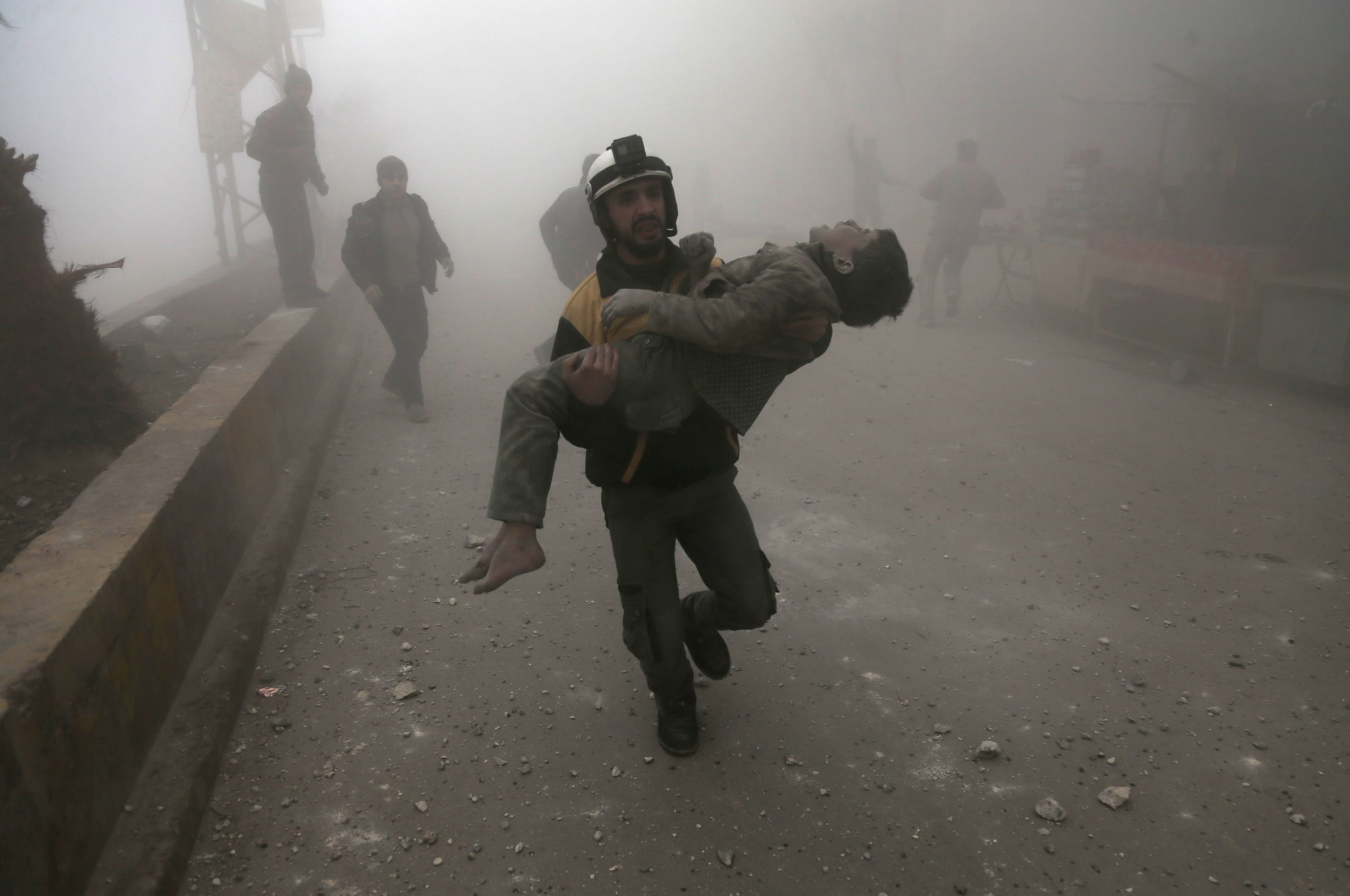 A White Helmet carries a wounded boy he'd helped dig out of the rubble following a January air strike on Hamouria, Syria (Abdulmonam Eassa/AFP/Getty Images)