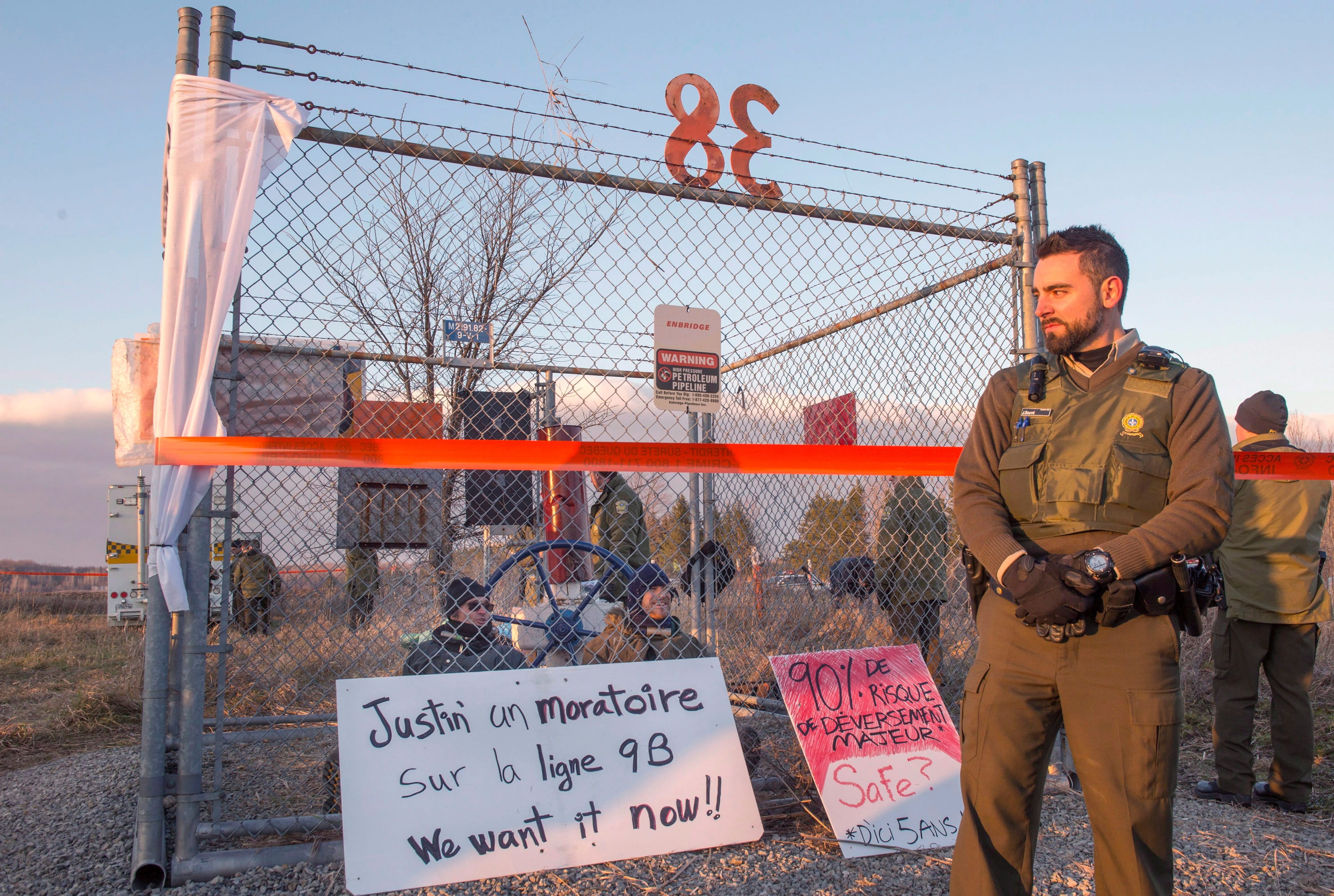 Police watch over two demonstrators locked to a valve along Enbridge pipeline 9B on Dec. 7, 2015, in Ste-Justine-de-Newton, Que. (THE CANADIAN PRESS/Paul Chiasson)