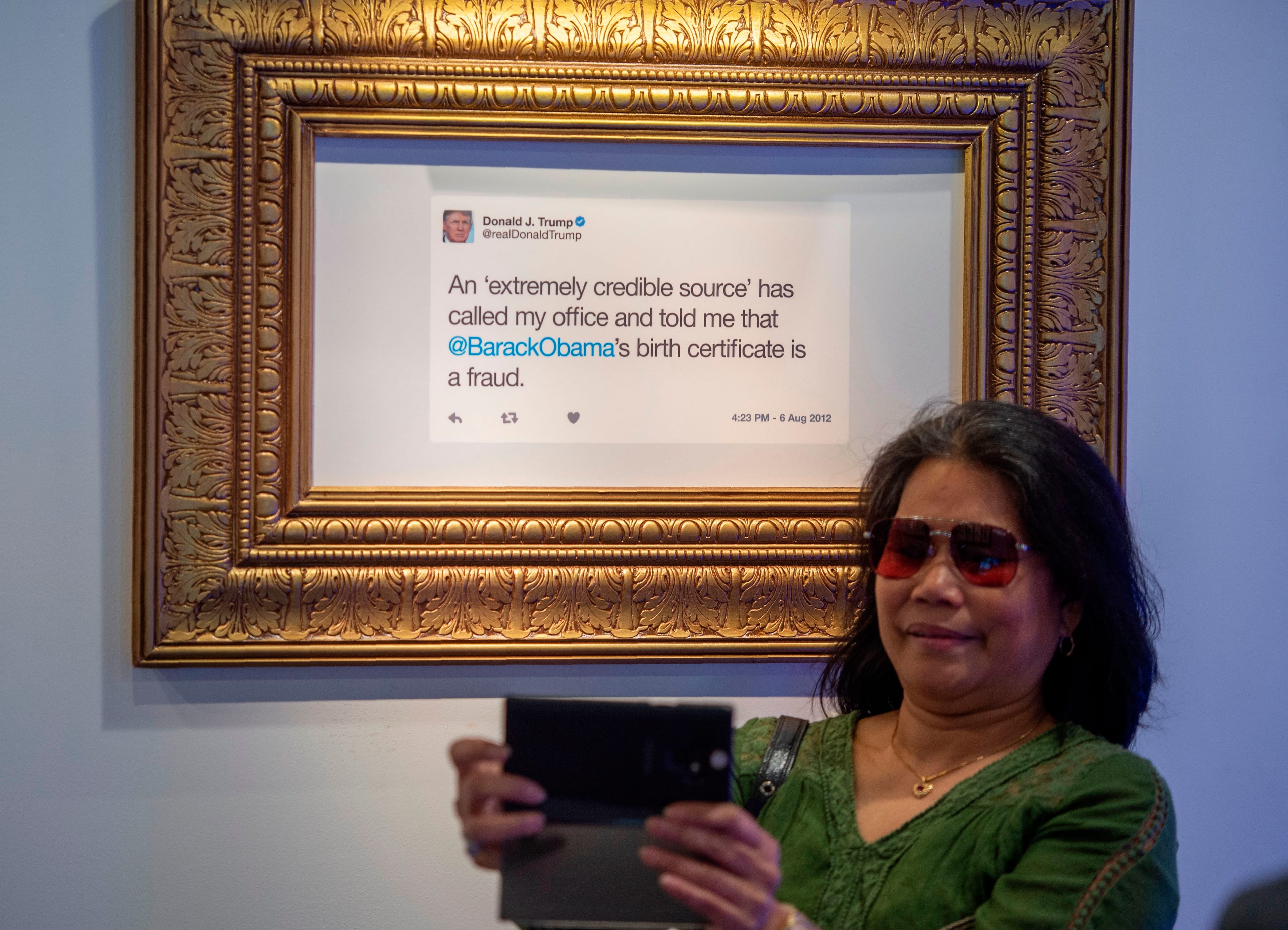 A visitor takes a selfie near a framed tweet by US President Donald Trump at "The Daily Show Presents: The Donald J. Trump Presidential Twitter Library" exhibition in Washington, DC on June 14, 2019. (Andrew Caballero-Reynolds/AFP/Getty)