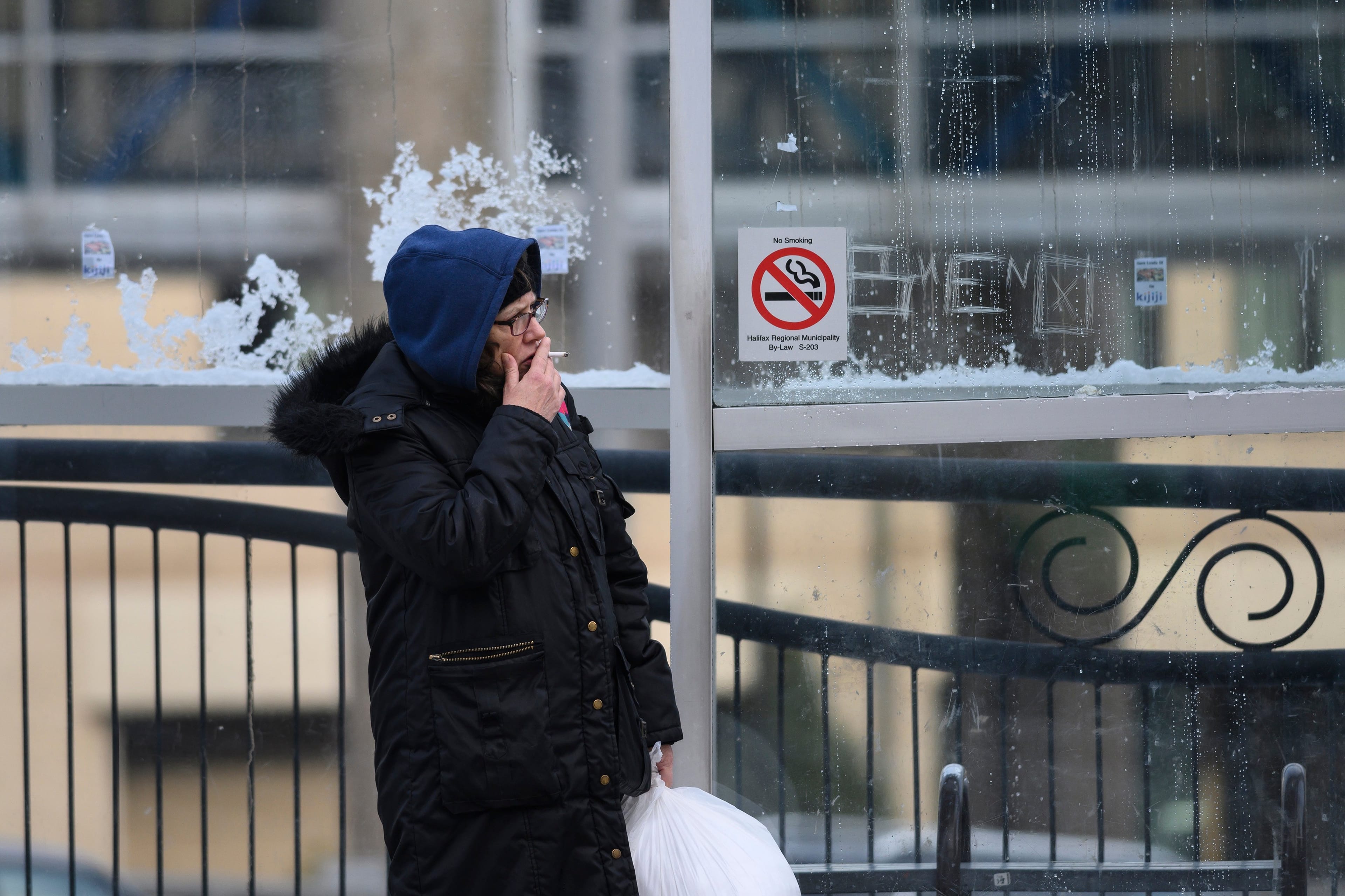 A woman smokes while waiting for the bus in downtown Halifax despite the city's by-law banning the act (Photograph by Darren Calabrese)