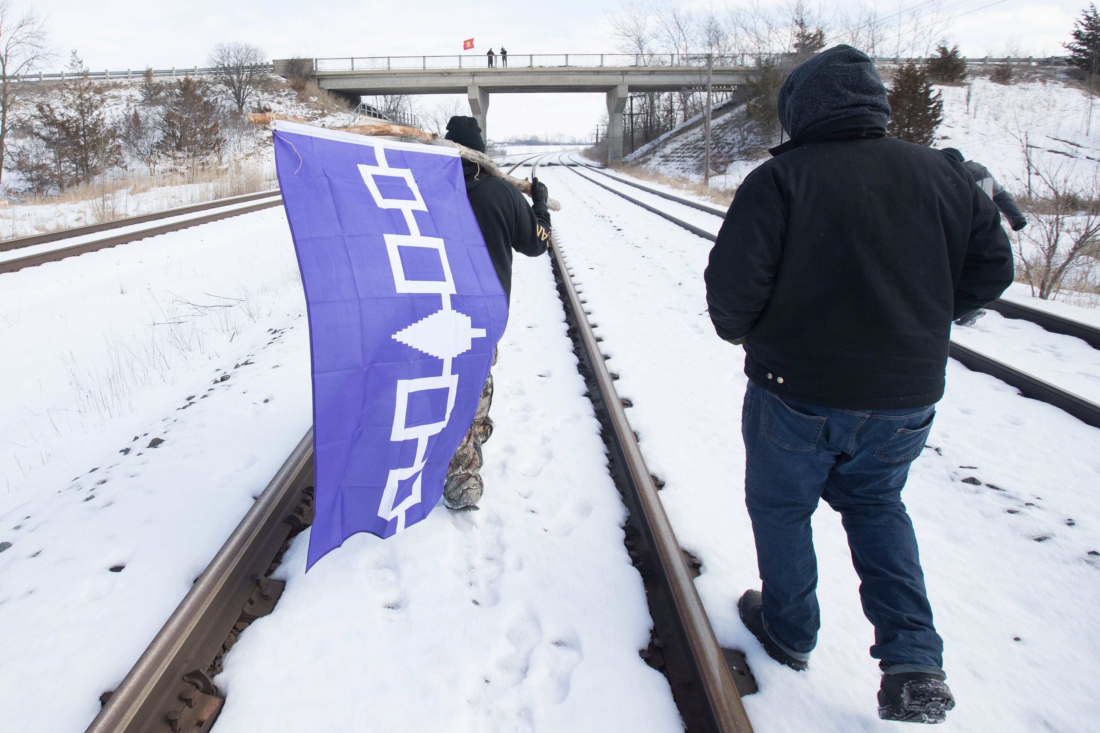 A man carries the Six Nations flag on the closed train tracks in Tyendinaga Mohawk Territory, Ont. on Wednesday, Feb. 12, 2020, in support of Wet'suwet'en's blockade of a natural gas pipeline in northern B.C. (Lars Hagberg/CP)