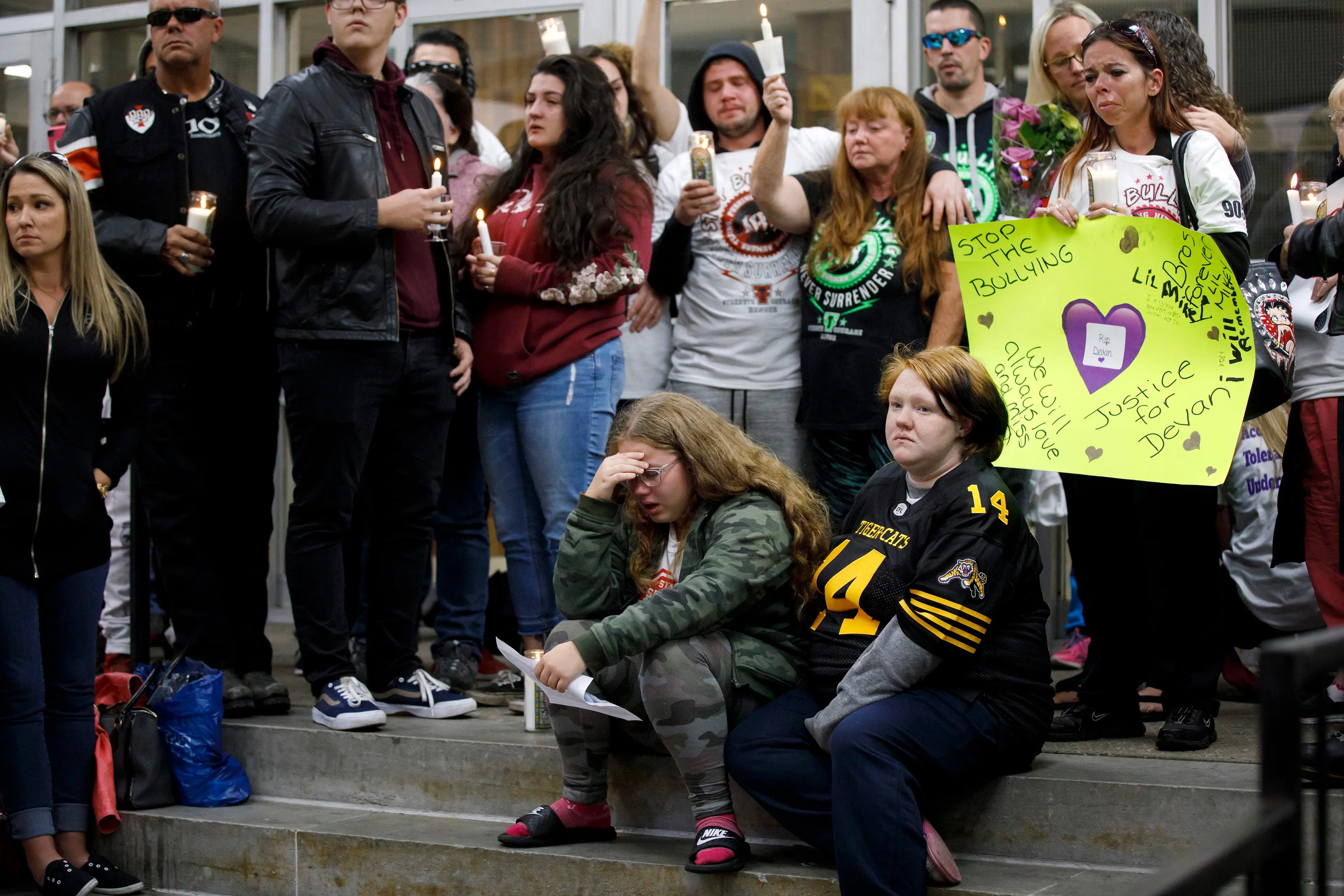 Devan Selvey’s girlfriend Danielle, seated left, his sister Karissa, seated right, and mother Shari-Ann, centre holding candle, attend a vigil for the murdered teen outside Sir Winston Churchill Secondary School, in Hamilton, Ontario, on Wednesday, Oct. 9, 2019. (Cole Burston/CP)