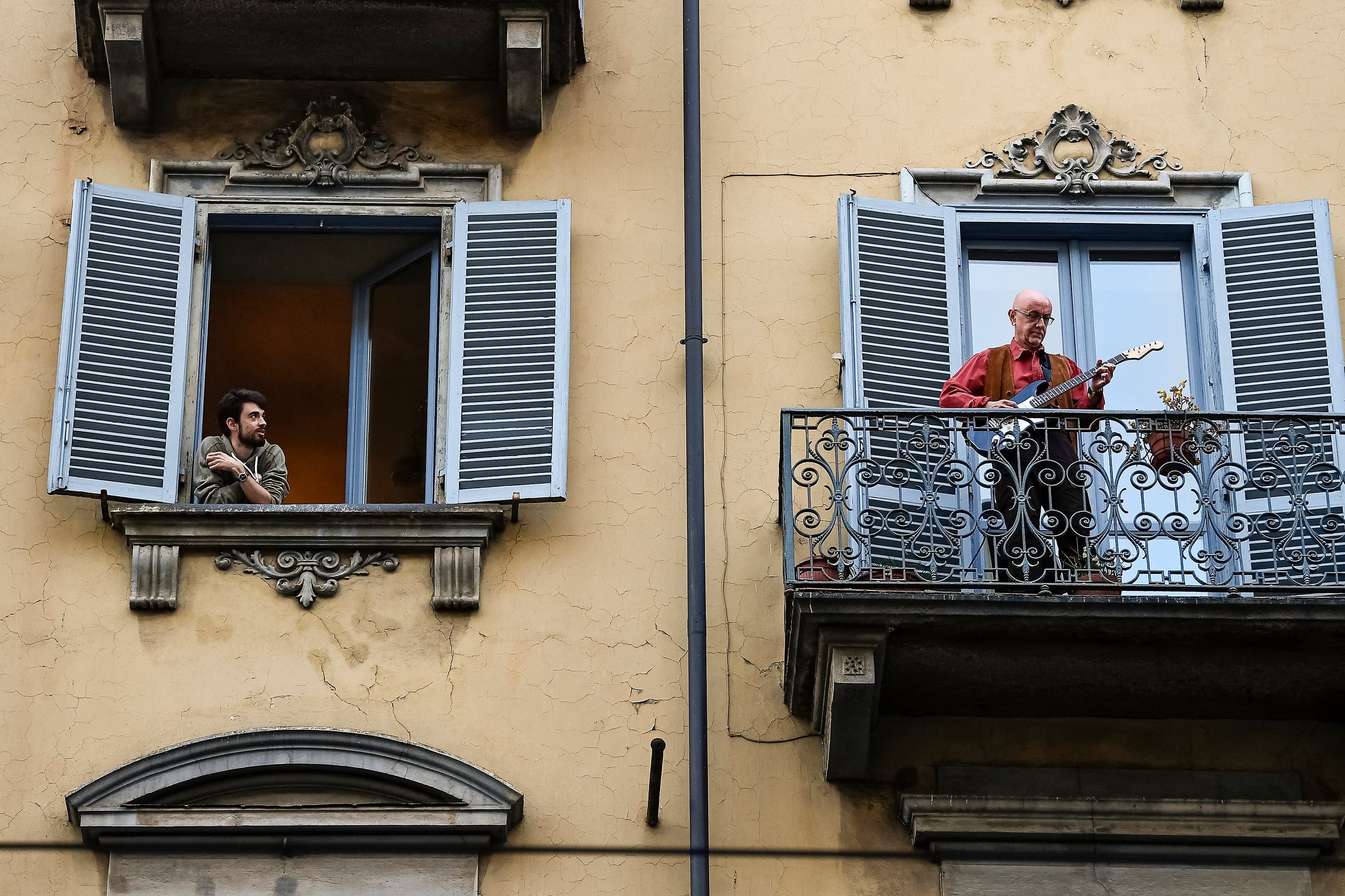 A man plays guitar from the balcony of his home as a man looks at him in the neighborhood San Salvario during a flash mob launched throughout Italy to bring people together during coronavirus. (Photo by Nicolò Campo/LightRocket/Getty Images)