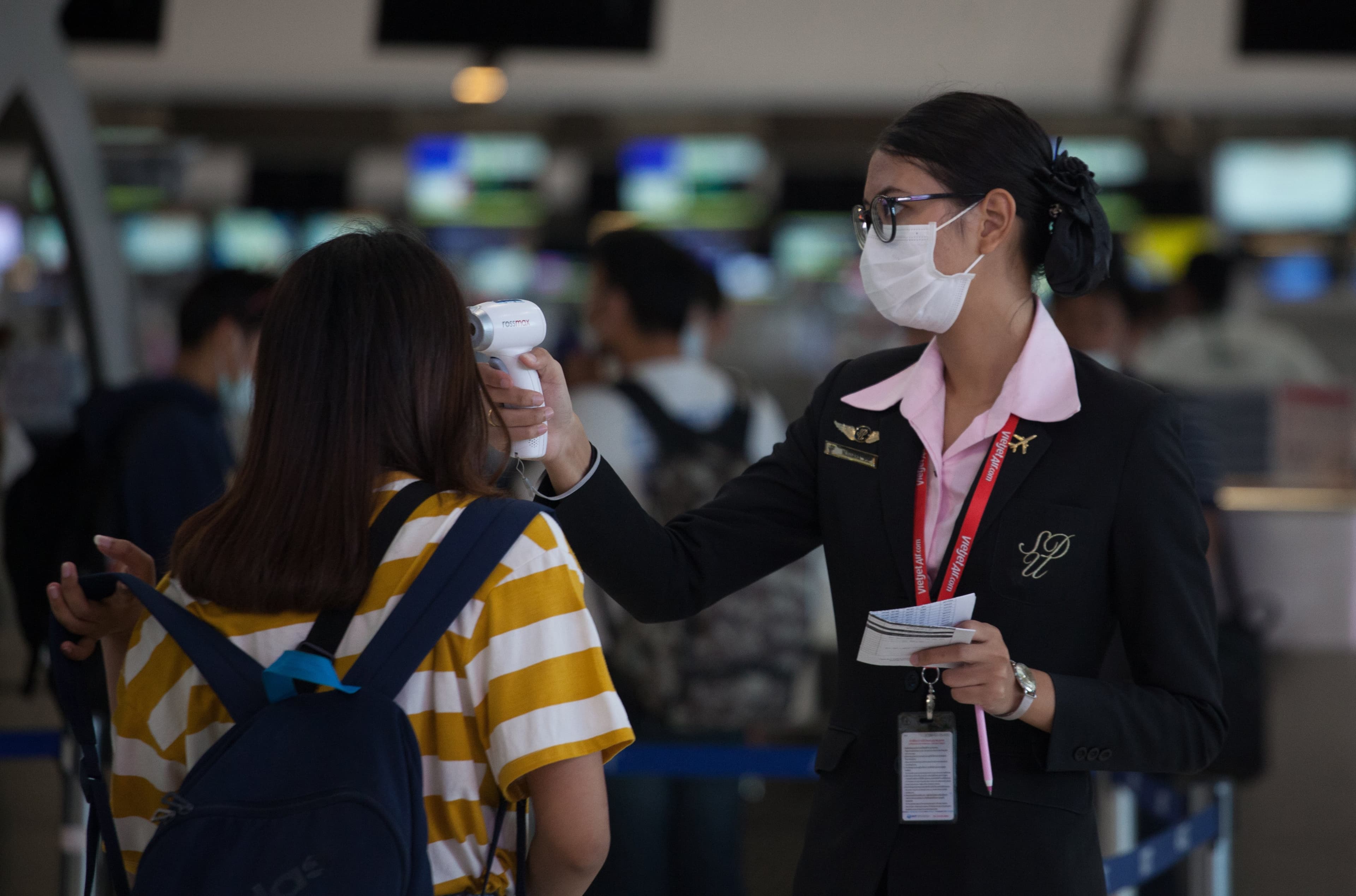 Airport receptionist wearing a face mask as a protective measure against the corona virus checks the body temperature a tourist at Suvarnabhumi airport.