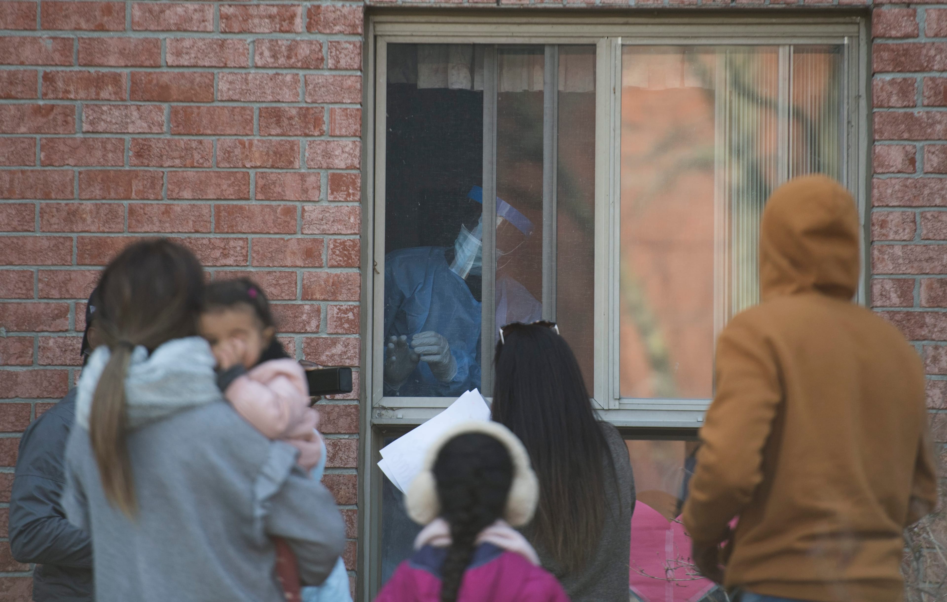 A health-care worker opens a window to a room at a long-term care home as family members of the resident look on in Montreal, on Apr. 25, 2020 (Graham Hughes/CP)