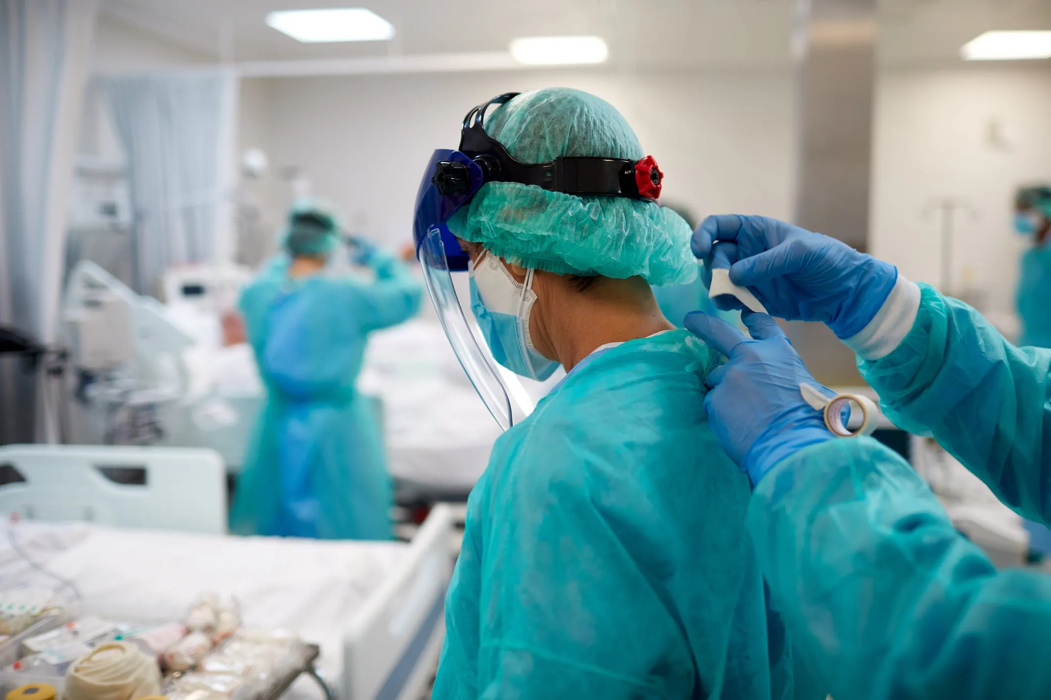 A nurse is helping her partner tie up the PPE coat in ICU
