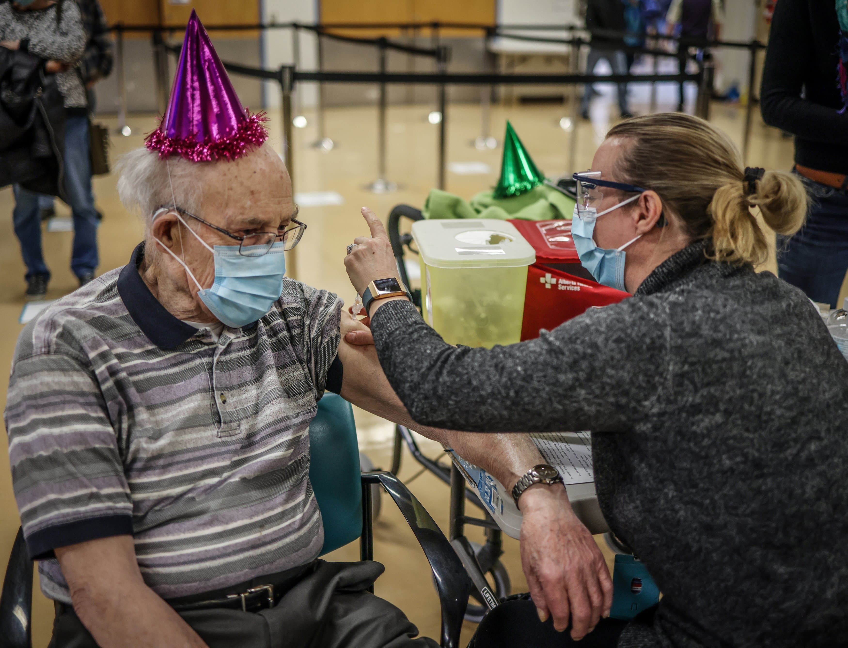 Karl Kuhnlein, 90, wears a party hat to receive his vaccination on Feb. 25 in Calgary; he’s looking forward to playing pool with friends (Leah Hennel/Alberta Health Services)