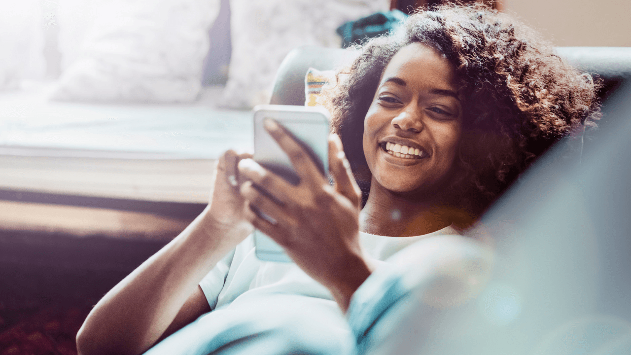 Happy woman using mobile phone on sofa