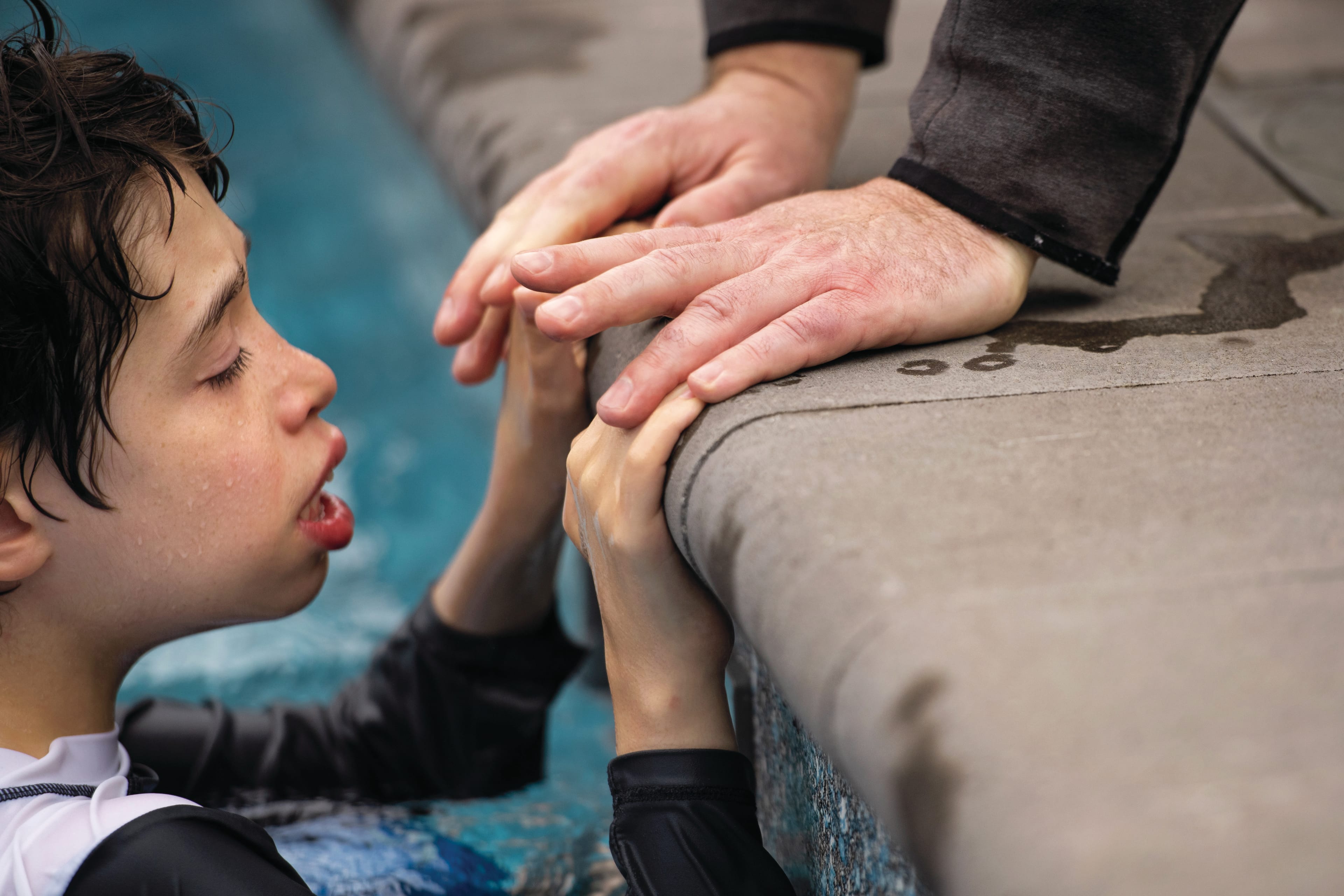 Libralesso’s father touches his son’s hands as he goes for a swim in his backyard in Barrie, Ont. (Photograph by Marta Iwanek)