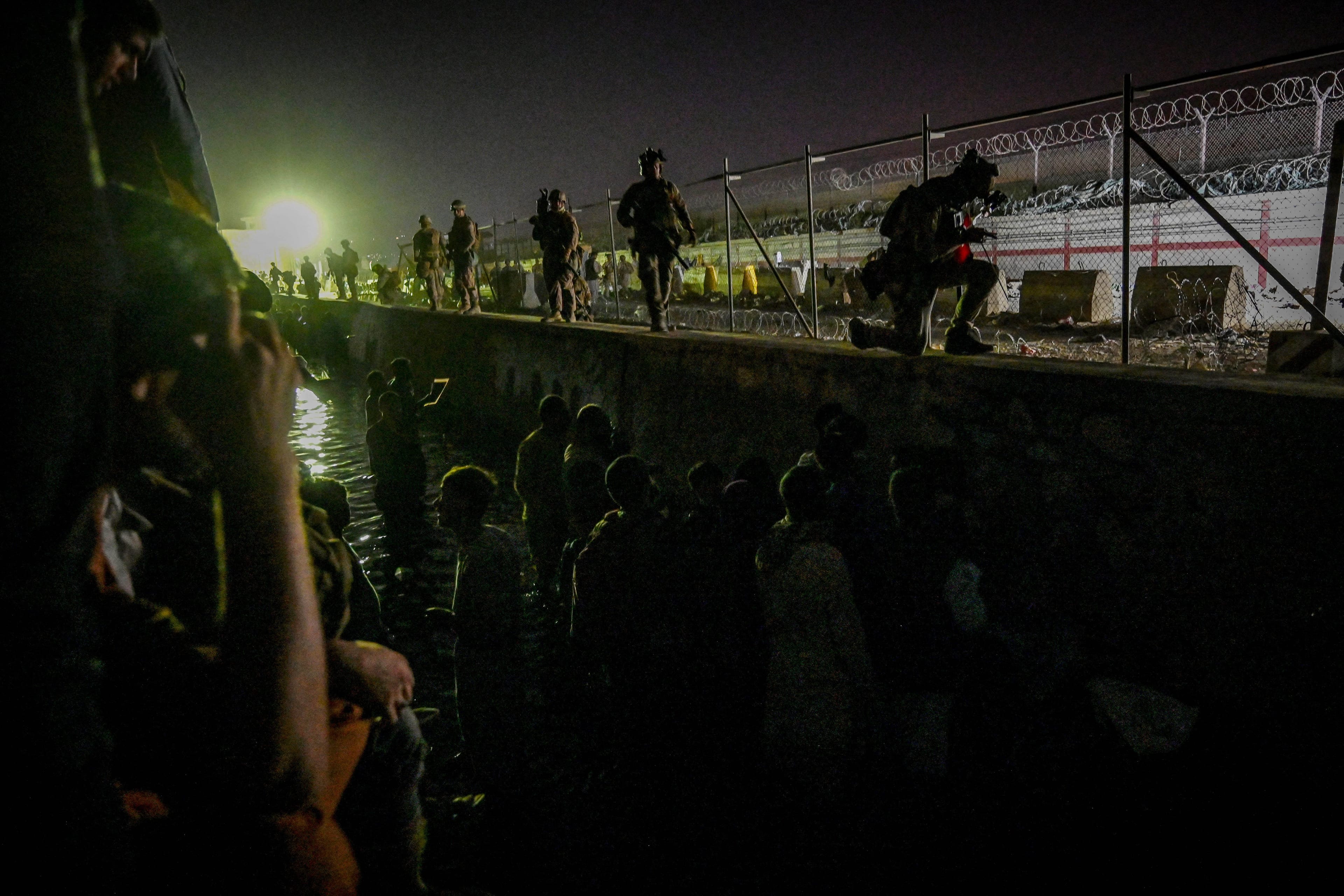 In this picture taken in the late hours on August 22, 2021 British and Canadian soldiers stand guard near a canal as Afghans wait outside the foreign military-controlled part of the airport in Kabul, hoping to flee the country following the Taliban's military takeover of Afghanistan. (Wakil Koshar/AFP/Getty Images)